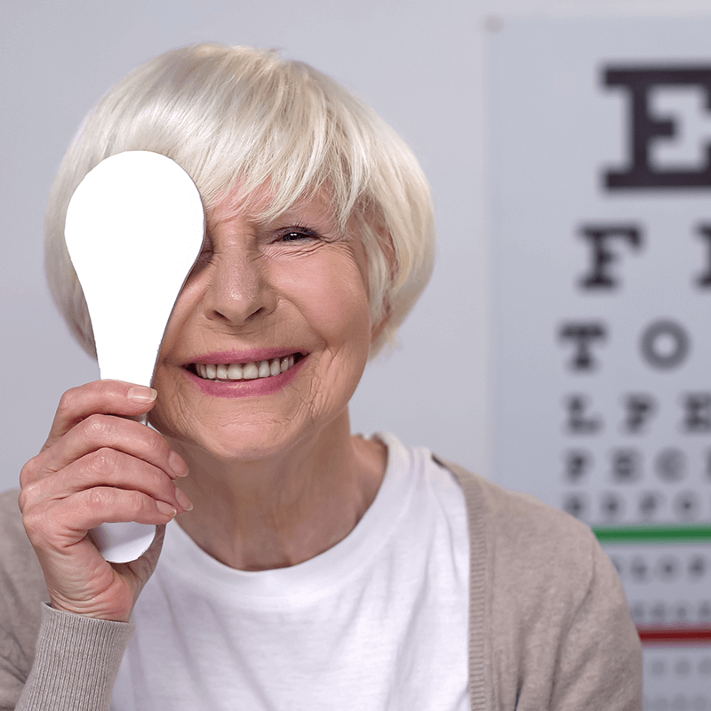 Smiling senior woman undergoing a vision test with an occluder at an eye clinic near me.