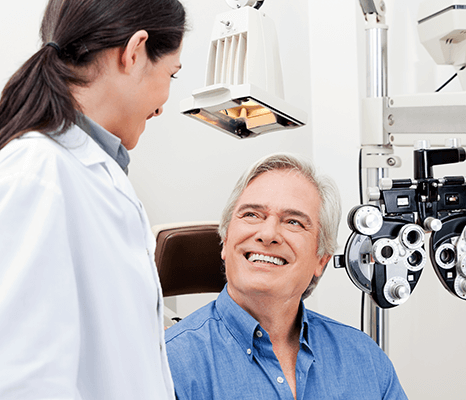 An eye doctor or ophthalmologist providing eye care to a smiling senior patient during an eye exam with an optometrist's equipment. Find an eye doctor near me or eye specialist near me for comprehensive eye care.